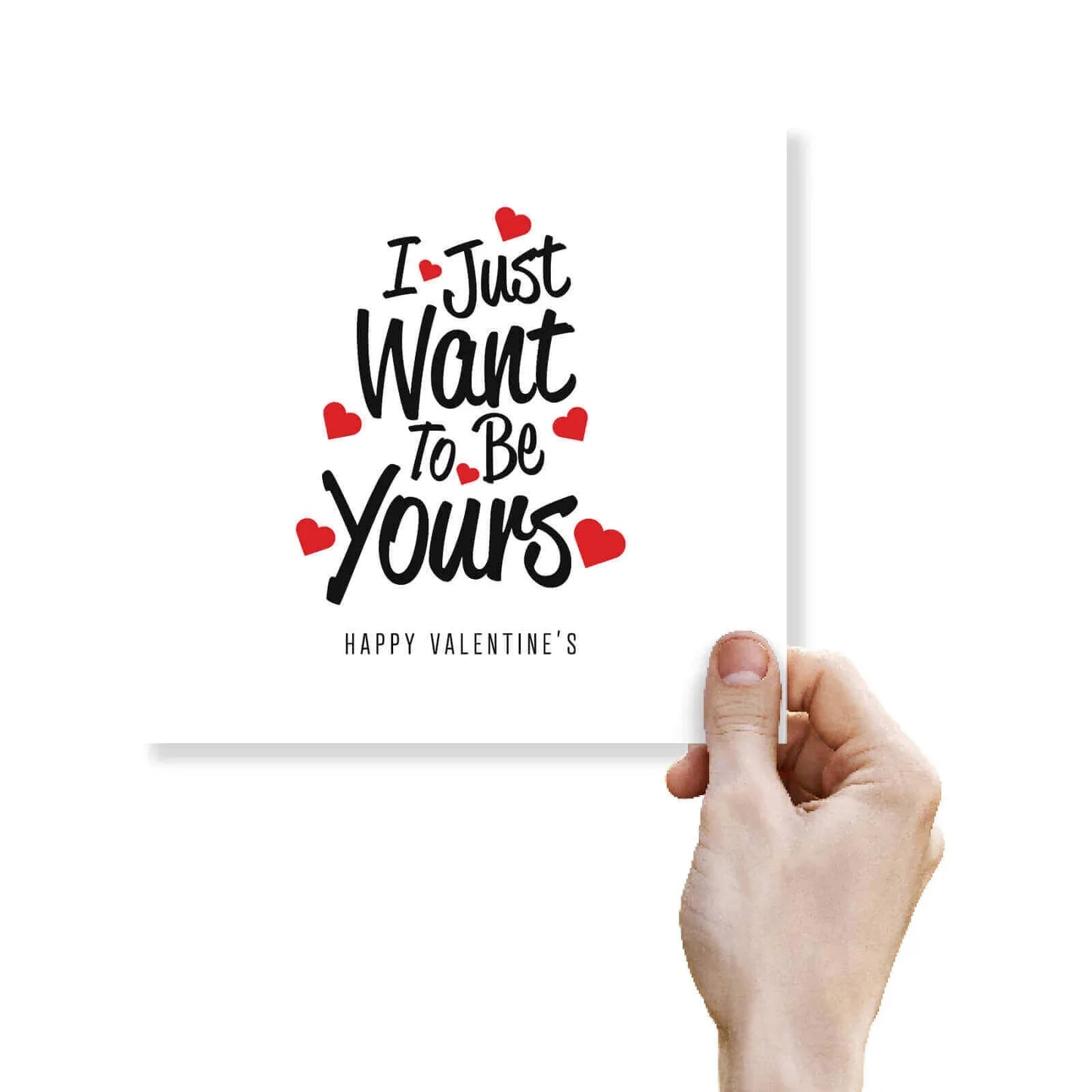 Hand holding a funny Valentine's greeting card with 'I just want to be yours' and red hearts.