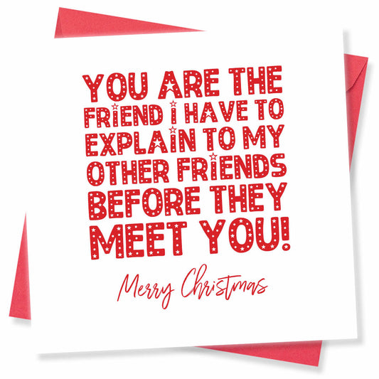 A square white Christmas greeting card with red text reading 'YOU ARE THE FRIEND I HAVE TO EXPLAIN TO MY OTHER FRIENDS BEFORE THEY MEET YOU! Merry Christmas', shown with red envelopes behind it on a white background.
