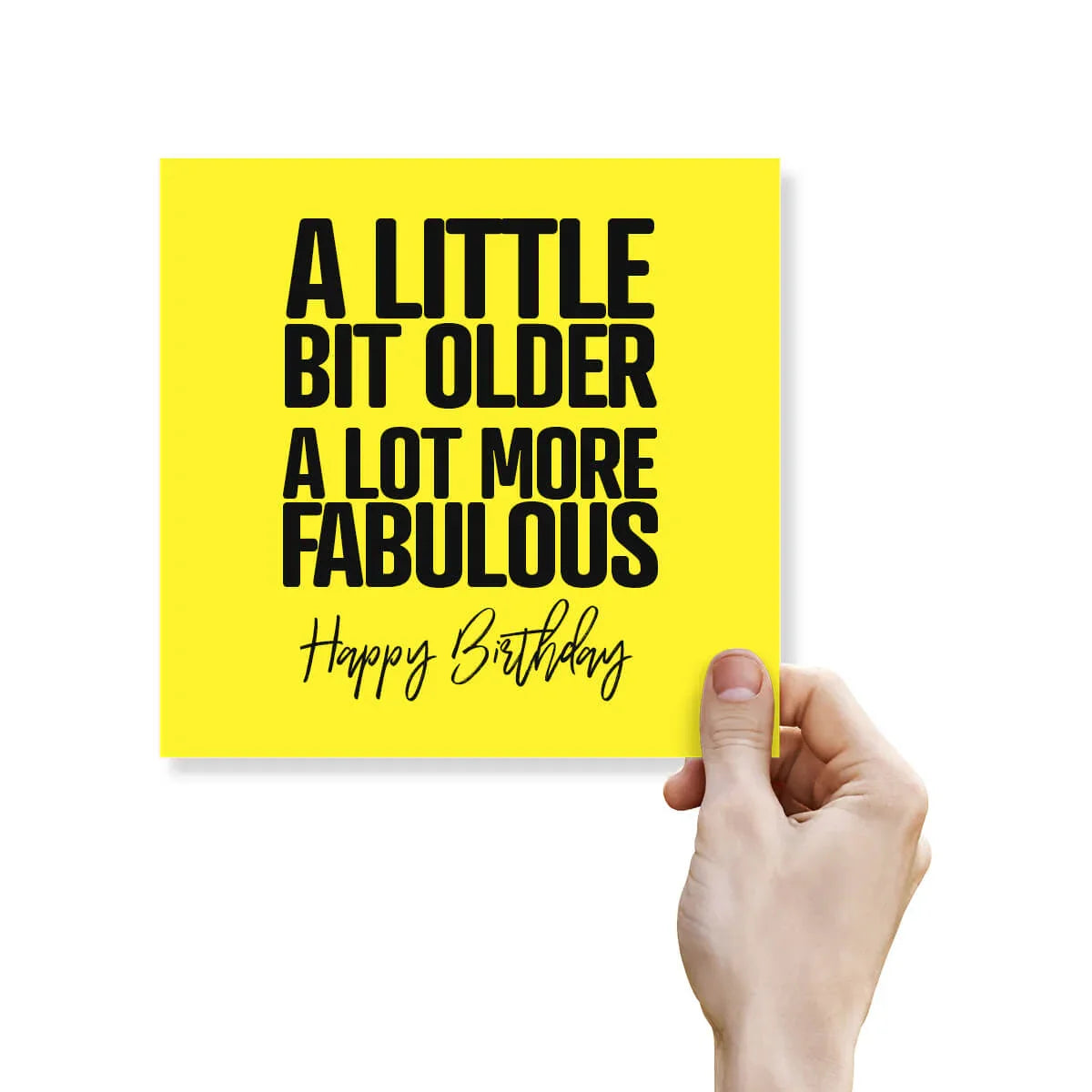 Funny yellow birthday card with bold black text reading 'A little bit older a lot more fabulous' held by a hand.