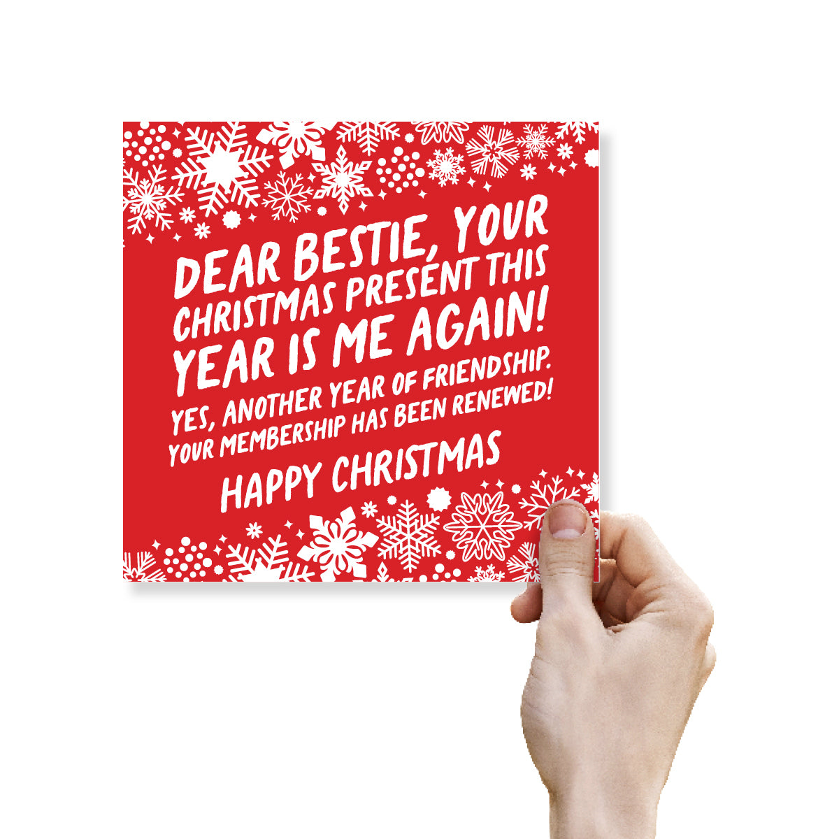 A hand holding a square red Christmas greeting card with white snowflake patterns and white text that reads, 'DEAR BESTIE, YOUR CHRISTMAS PRESENT THIS YEAR IS ME AGAIN! YES, ANOTHER YEAR OF FRIENDSHIP, YOUR MEMBERSHIP HAS BEEN RENEWED! HAPPY CHRISTMAS' on a white background.