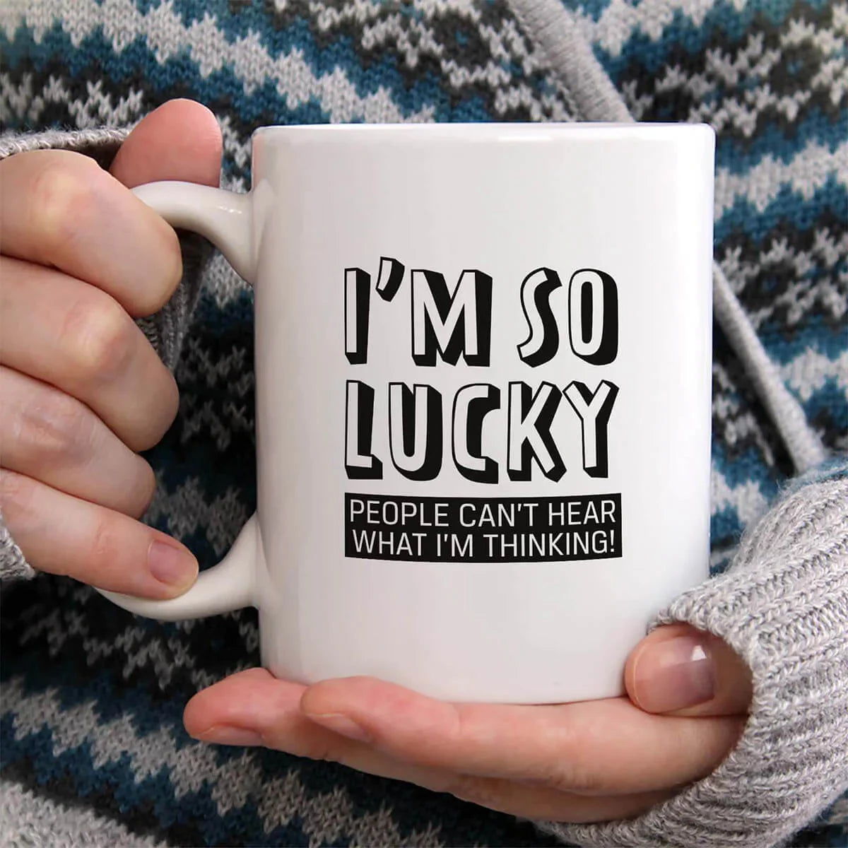 Person holding a white mug with text 'I'm so lucky people can't hear what I'm thinking' against a patterned background.