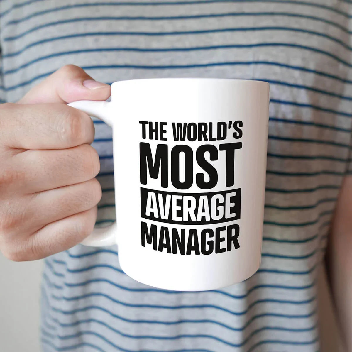 Funny coffee mug with the text 'The World's Most Average Manager' held by person in striped shirt