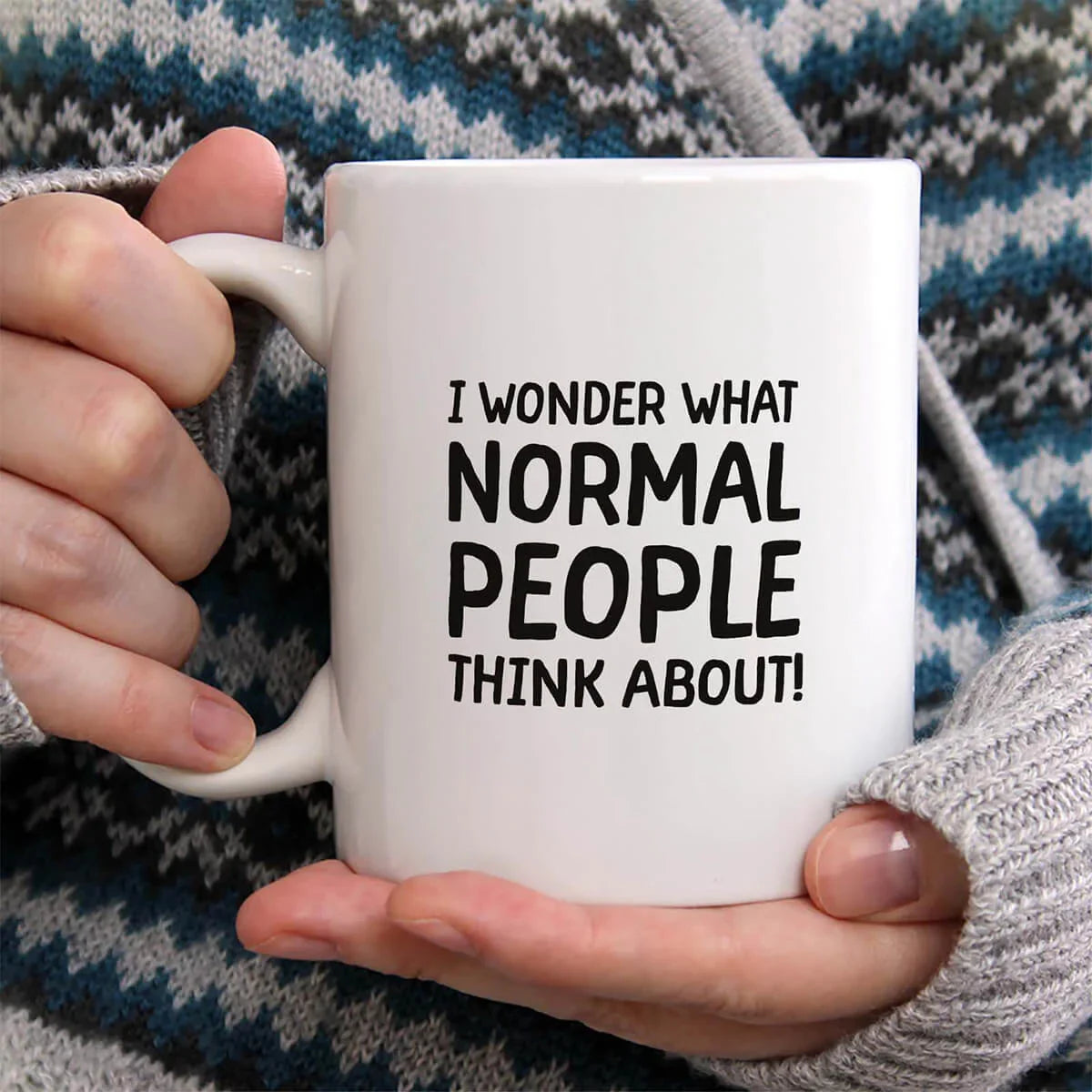 Person holding a white mug with text 'I wonder what normal people think about!' against a patterned background.