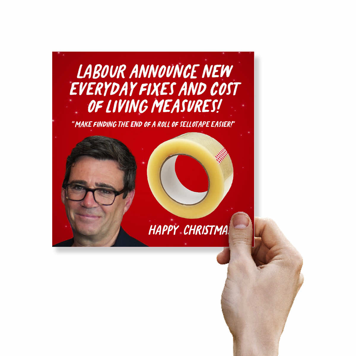 A hand holding a square red novelty card or poster featuring white text, a photo of a man with glasses, and a roll of yellow tape. The card reads, 'LABOUR ANNOUNCE NEW EVERYDAY FIXES AND COST OF LIVING MEASURES! MAKE FINDING THE END OF A ROLL OF SELLTAPE EASIER! HAPPY CHRISTMAS'.